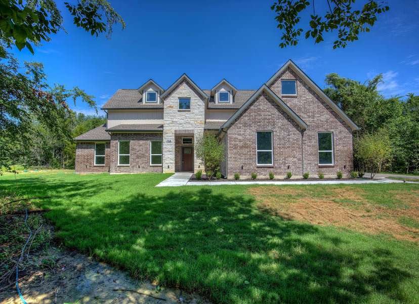 Custom two-story home exterior in Terrell — brick and stone facade with dark shingle roof and landscaped lawn